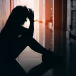 Silhouette of sad and depressed woman sitting at walkway of condominium or office with backlit and lens flare
