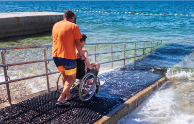 a person pushing a Man in wheelchair on accessible beach with ramp.