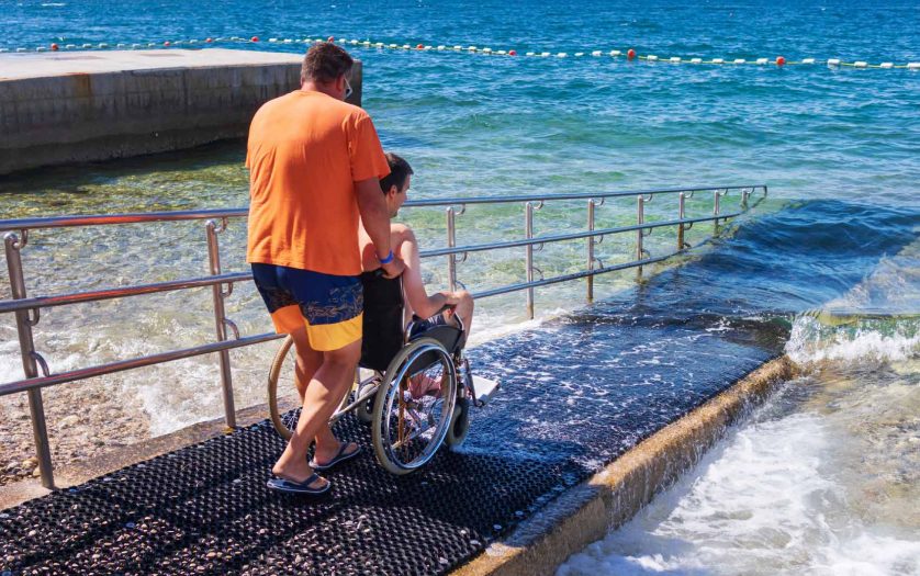 a person pushing a Man in wheelchair on accessible beach with ramp.