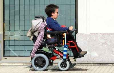 A young woman in a wheelchair, walking along a sidewalk in the city.