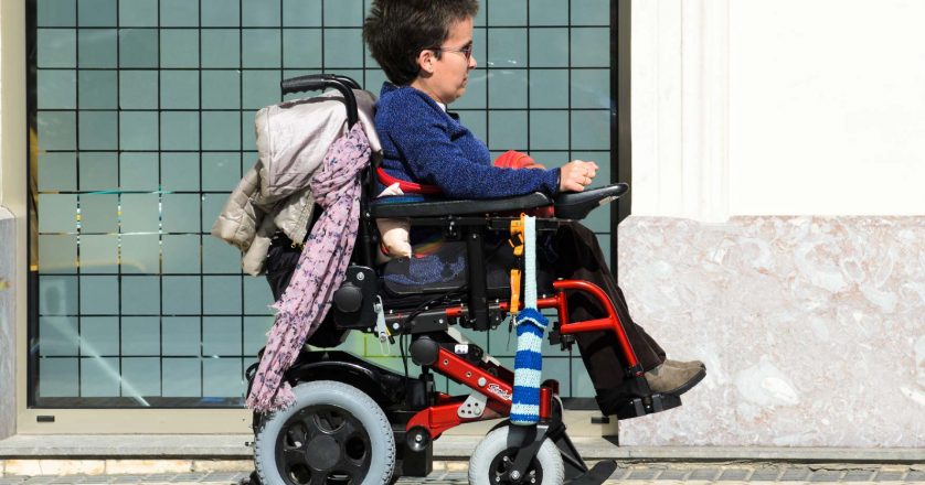 A young woman in a wheelchair, walking along a sidewalk in the city.