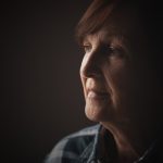Close-up portrait of senior woman with dementia who is looking through window.