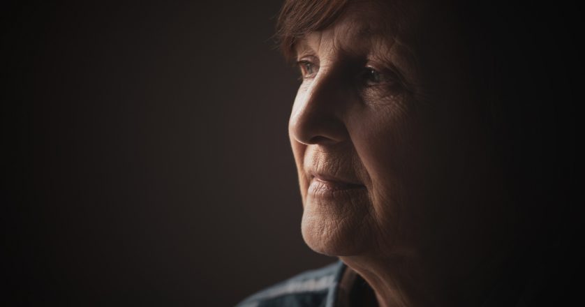 Close-up portrait of senior woman with dementia who is looking through window.