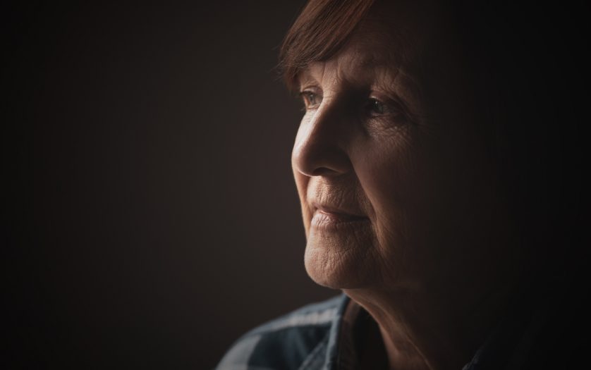 Close-up portrait of senior woman with dementia who is looking through window.