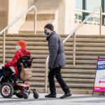 Person in wheelchair with a man walk into Metro Convention Centre vaccination centre to receive their COVID-19 vaccine.
