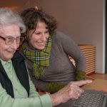Young women and senior women sitting together watching at photos on the screen of a notebook