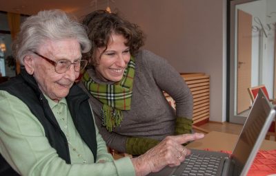 Young women and senior women sitting together watching at photos on the screen of a notebook