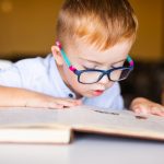 Cute kid with disability with big glasses reading book