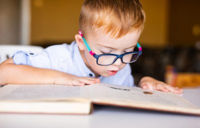Cute kid with disability with big glasses reading book