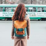 Young woman curly red head girl with backpack in front of tram at the city street