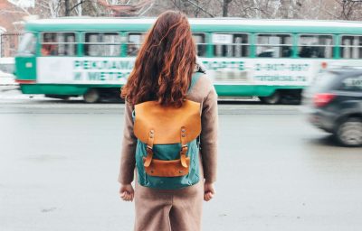 Young woman curly red head girl with backpack in front of tram at the city street