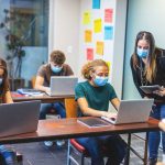 High School Students wearing masks and using computers in a classroom with social distancing measures