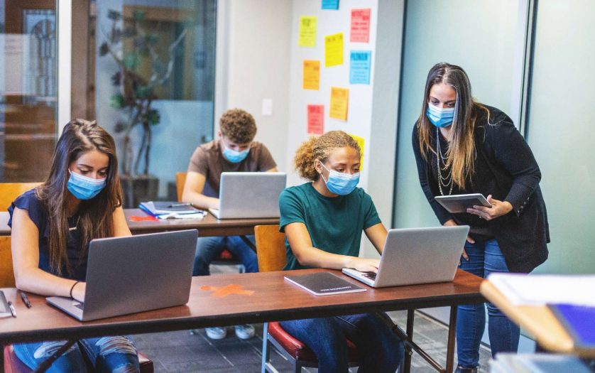 High School Students wearing masks and using computers in a classroom with social distancing measures