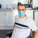 man in wheelchair wearing face mask sitting in front of kitchen.