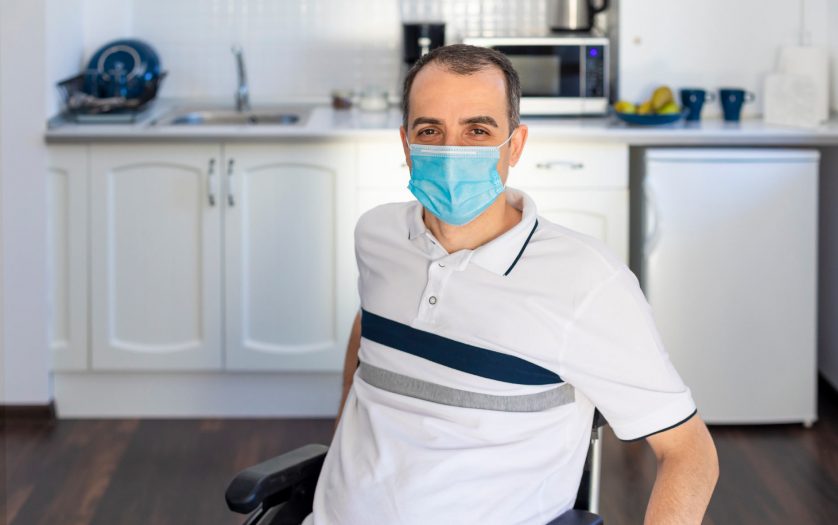man in wheelchair wearing face mask sitting in front of kitchen.