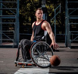 Basketball player in a wheelchair plays on an open gaming ground.