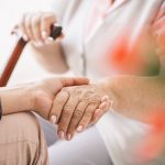 Close-up of young caregiver holding older woman's hand