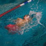 Quadriplegic swimmer in the water. He is using the back stroke technique in the pool lane