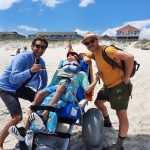 A wheelchair user with smiling people looking at camera outdoor