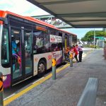 A bus driver lowers the ramp at the rear door for the helper to push a wheelchair bound passenger up onto the bus