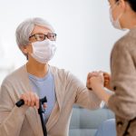 Care worker supporting a senior woman wearing facemasks