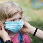 Parent fitting a face mask to a young blond girl as protection during the Covid-19