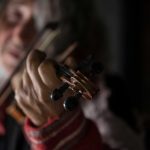 Close up of man playing music on a classical violin indoors.