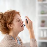 Woman sneezing while using inhalator because of asthma