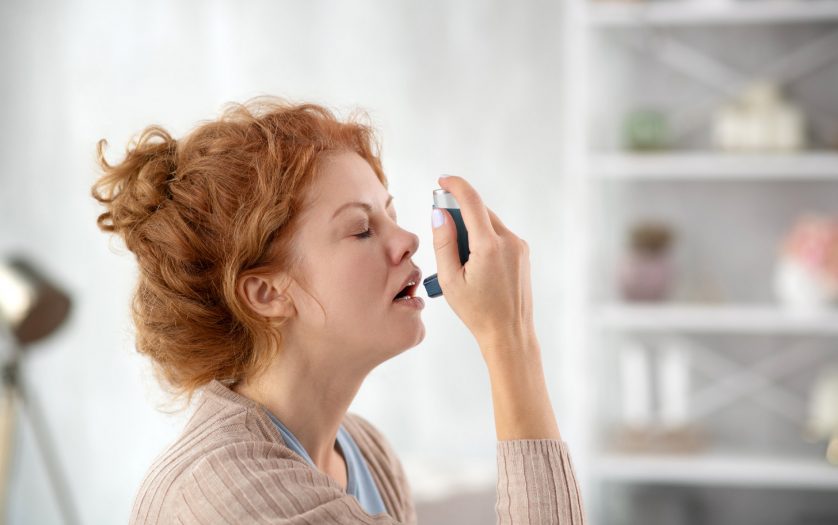 Woman sneezing while using inhalator because of asthma