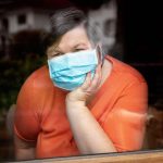 disabled woman with surgical mask looking out at window