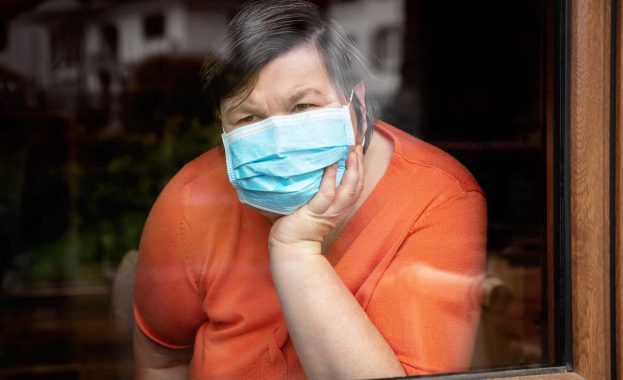 disabled woman with surgical mask looking out at window