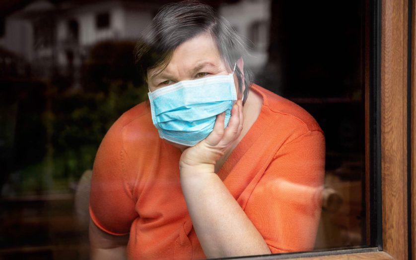 disabled woman with surgical mask looking out at window