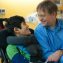 Smiling father sitting next to disabled son in wheelchair by hospital bed, talking together