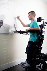 Boy writing on Blackboard while using standing wheelchair 