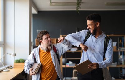 Young happy man with Down syndrome with his mentoring friend celebrating success