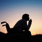 A silhouette of a senior woman in wheelchair in nature in the evening