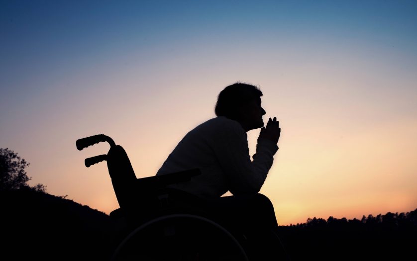 A silhouette of a senior woman in wheelchair in nature in the evening