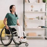 smiling disabled woman looking away while sitting in wheelchair at home