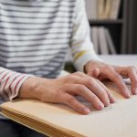 Close up of unrecognizable person reading braille book in college library