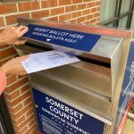 Woman dropping off her voting ballot into a ballot drop box