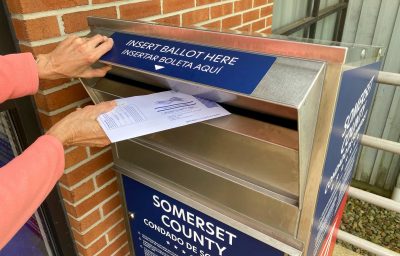 Woman dropping off her voting ballot into a ballot drop box