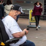 A disabled man wearing a mask sitting in his wheelchair is checking his phone