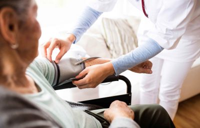 A nurse checking blood pressure of a woman in an wheelchair.