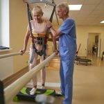 woman walking between parallel bars at rehabilitation room