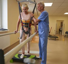woman walking between parallel bars at rehabilitation room
