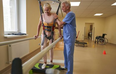 woman walking between parallel bars at rehabilitation room