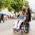 Assistant helping disabled woman in wheelchair move around city