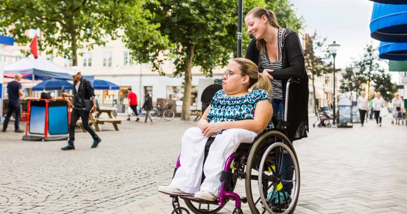 Assistant helping disabled woman in wheelchair move around city