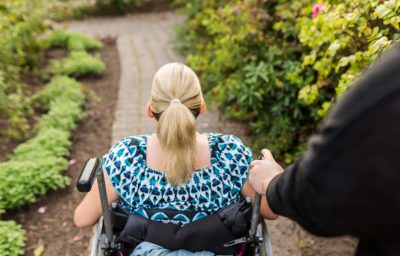 Disabled woman in wheelchair with assistant walking in garden