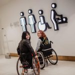 Two girls in wheelchairs near the entrance to the public toilet